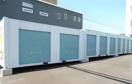 Line of blue storage containers with large roll-up doors in an urban outdoor setting, ideal for bulk storage