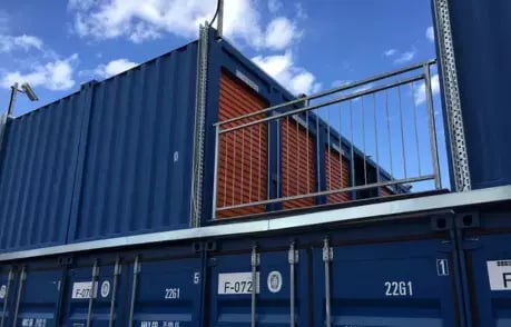 Elevated blue shipping container with an external staircase and balcony, designed for office or studio use.