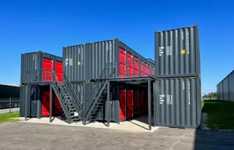 A compact, multi-level storage facility made from stacked 40 HC shipping containers, each self-storage unit features 8 storage rooms,featuring external staircases and secured red doors, set in a spacious outdoor area.