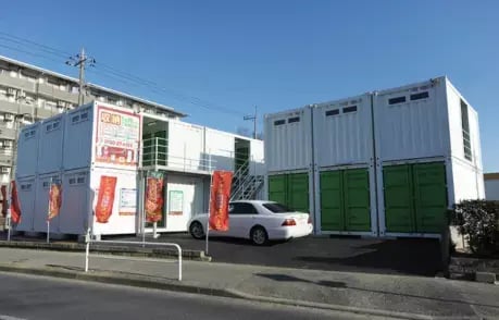 Stacked shipping containers in green and white, used for advertisement and storage, featuring swing doors and signage